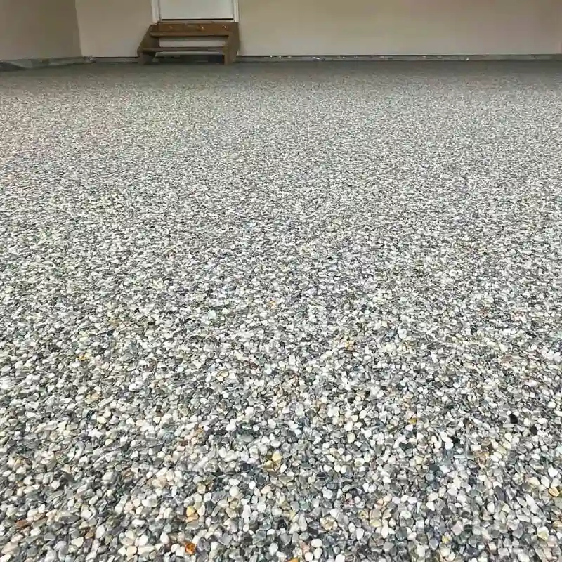 A freshly installed stone epoxy flooring system covers a large indoor space, possibly a garage or showroom.