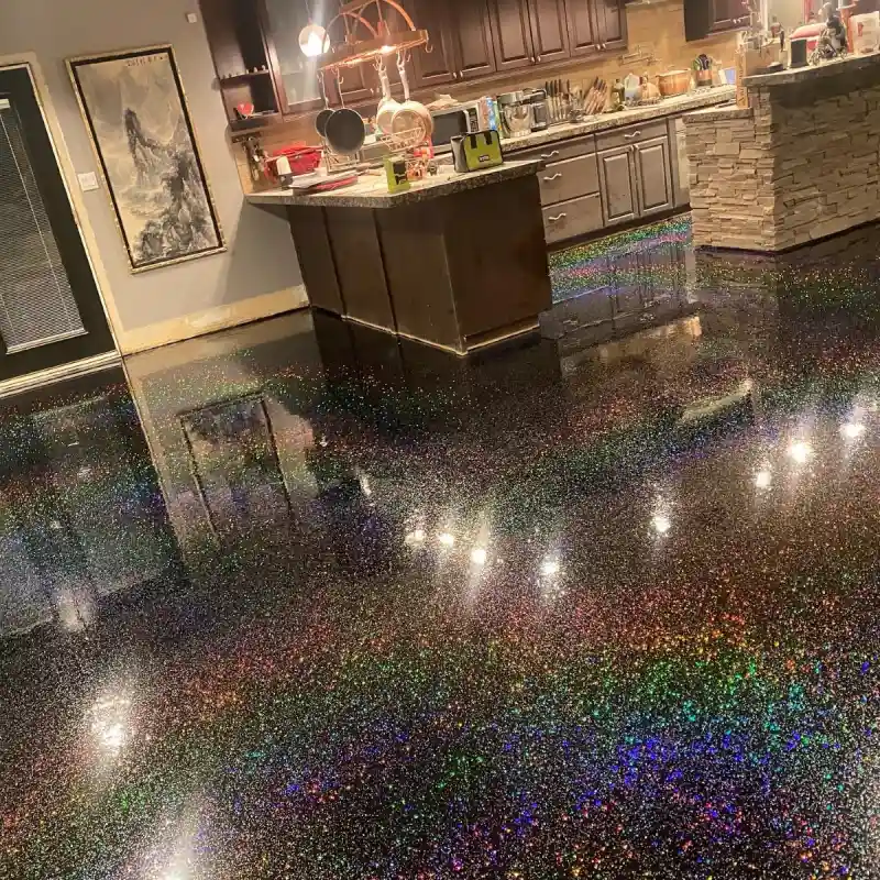 A modern kitchen features a striking glitter epoxy flooring system. The floor is a dark, highly reflective surface