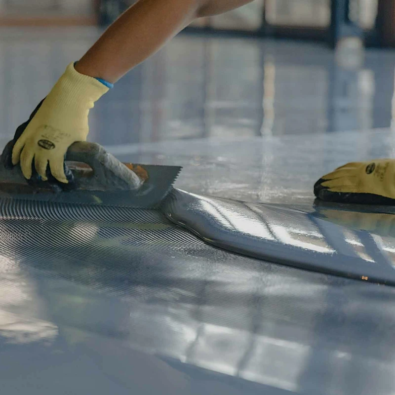 A professional installer wearing yellow gloves is applying a thick coat of vapor barrier epoxy flooring